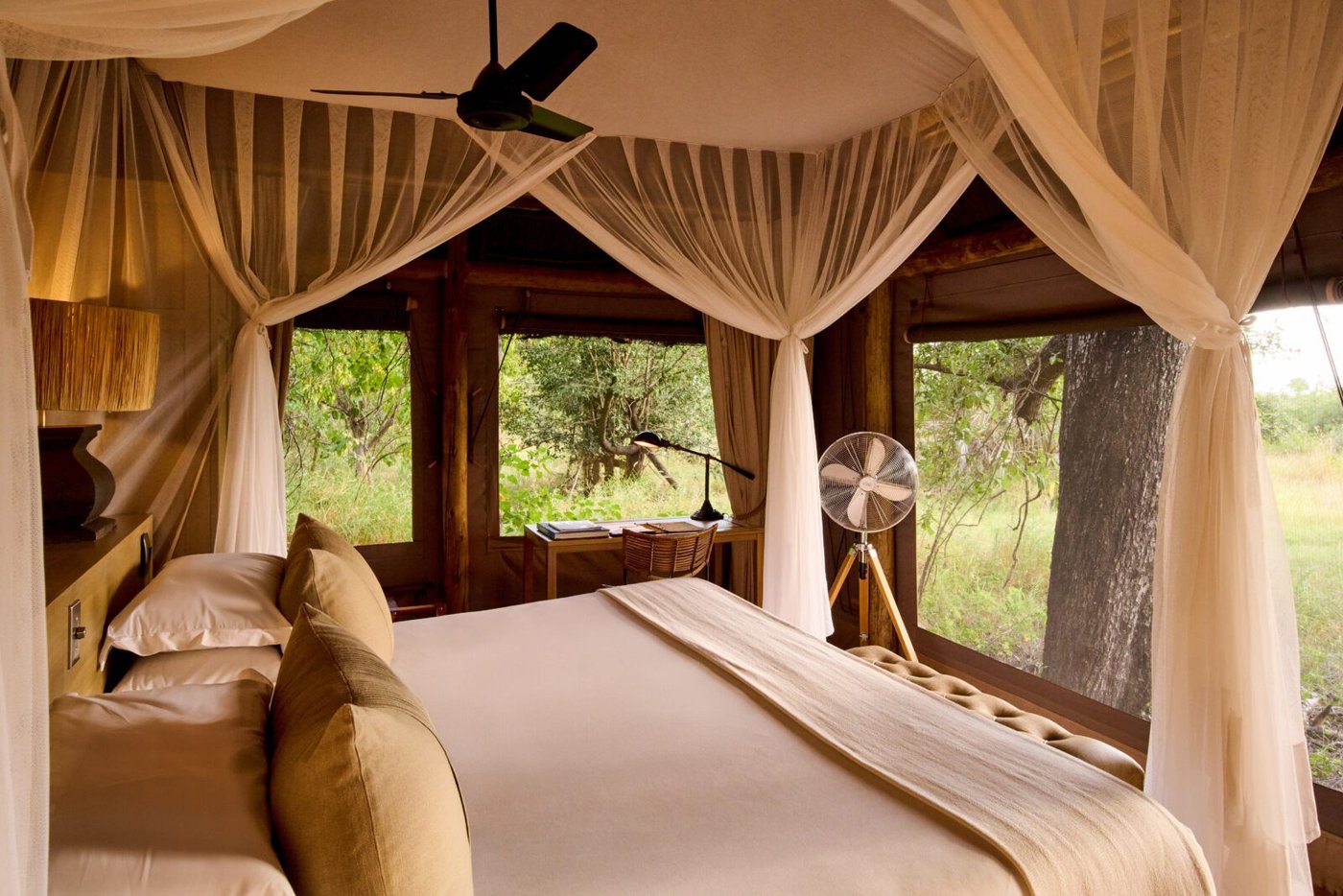 Netted four-poster bed in a Camp Moremi tent, its screen windows open to the bush