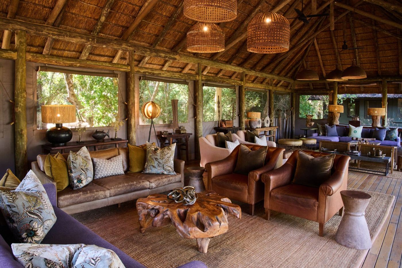 Leather armchairs and woven lamps in the Camp Moremi lounge, a canvas-walled room under thatch