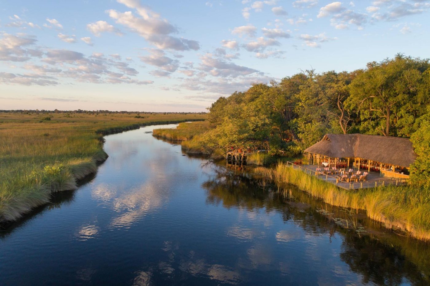 Camp Xakanaxa's thatched main deck beside a reed-lined channel of the Moremi floodplain, from the air