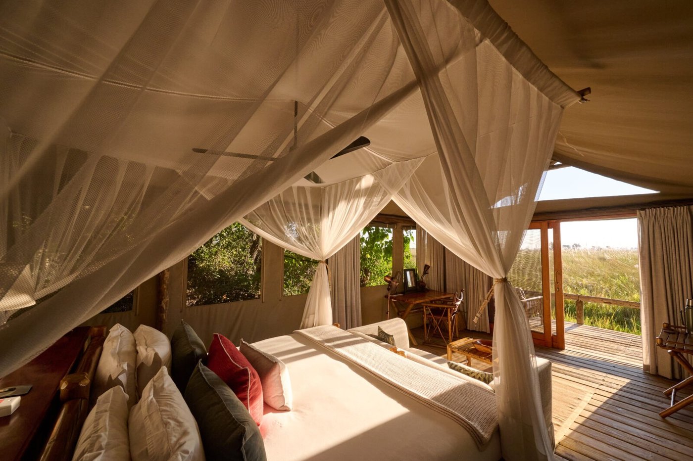 Netted bed and writing desk inside a Camp Xakanaxa tent, doors open onto the deck
