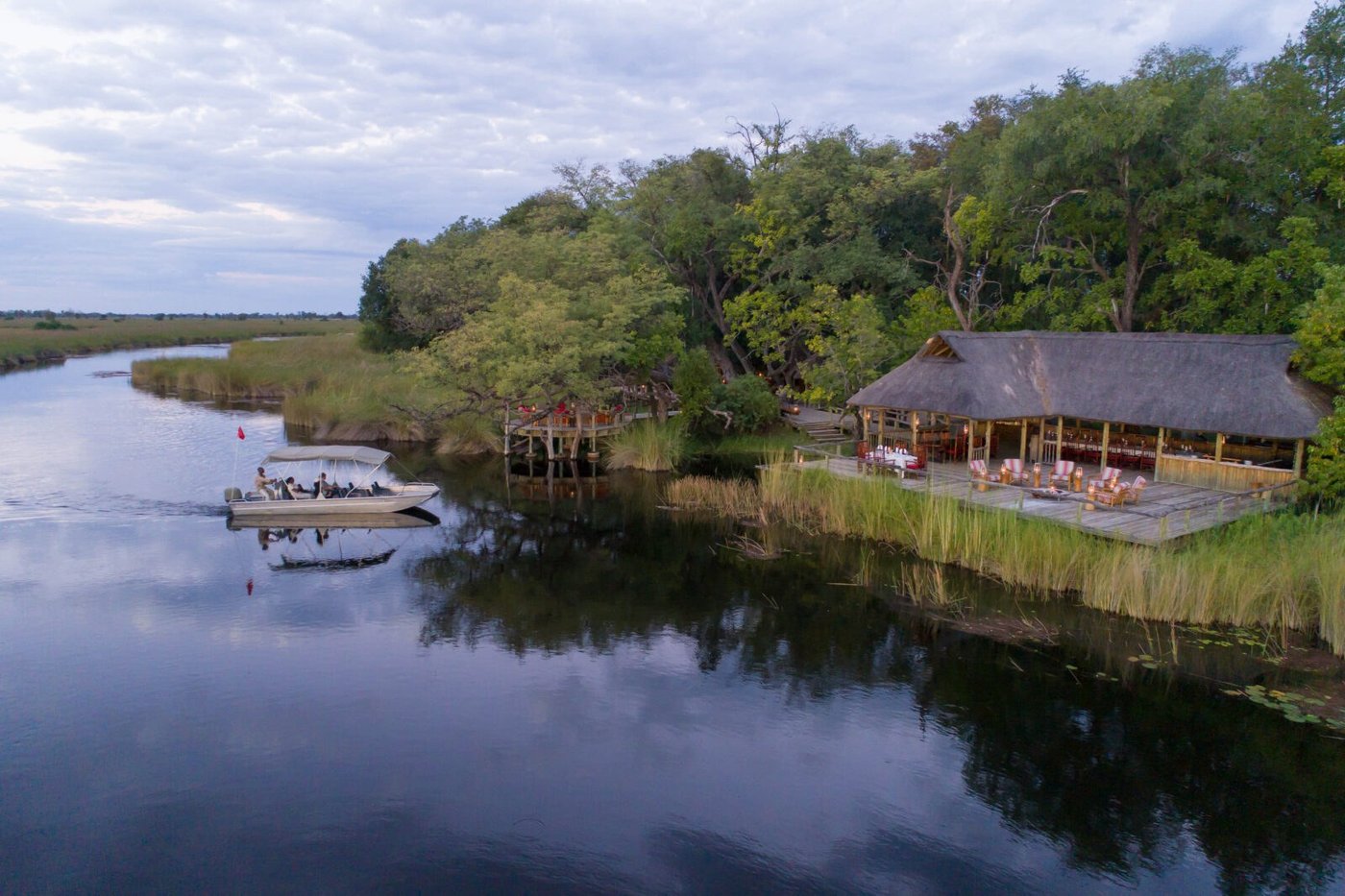 A motorboat heads out along the channel past the main deck of Camp Xakanaxa
