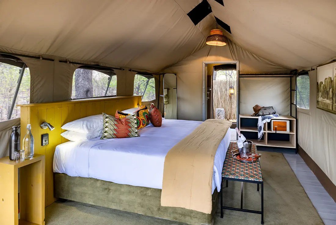 A double bed with a yellow headboard under canvas in an Elephant Pan guest tent