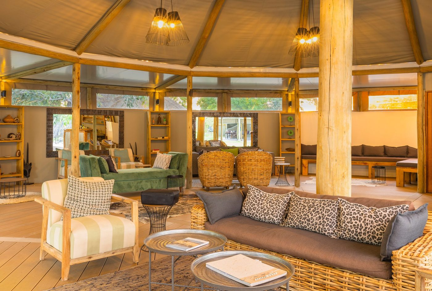 Wicker sofa, green daybed and bookshelves in the canvas-roofed lounge at Khwai Guest House