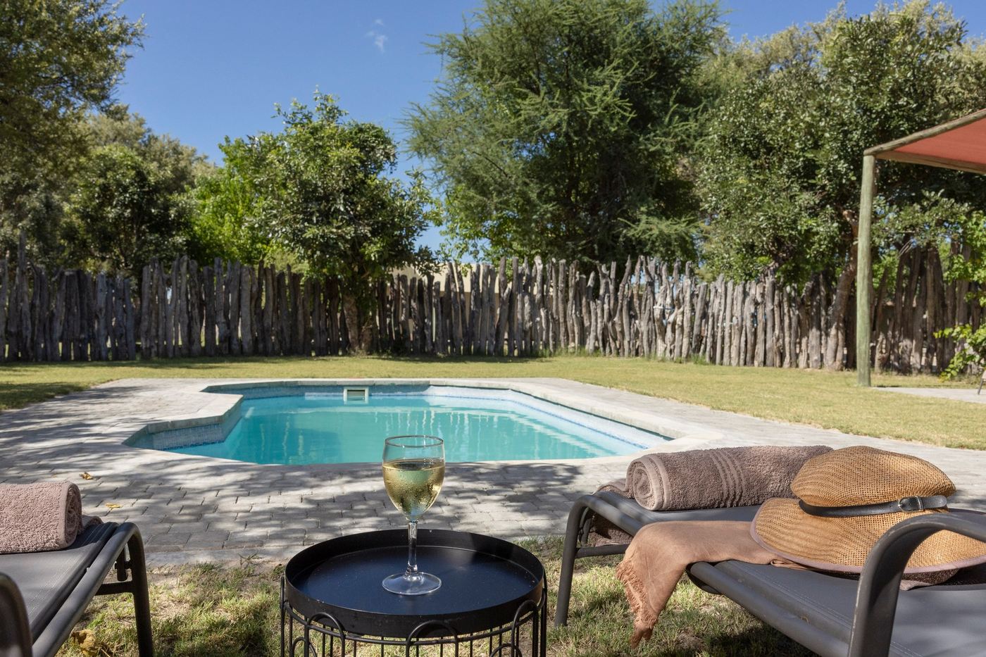 Swimming pool and shaded loungers inside the wooden pole fence at Khwai Guest House