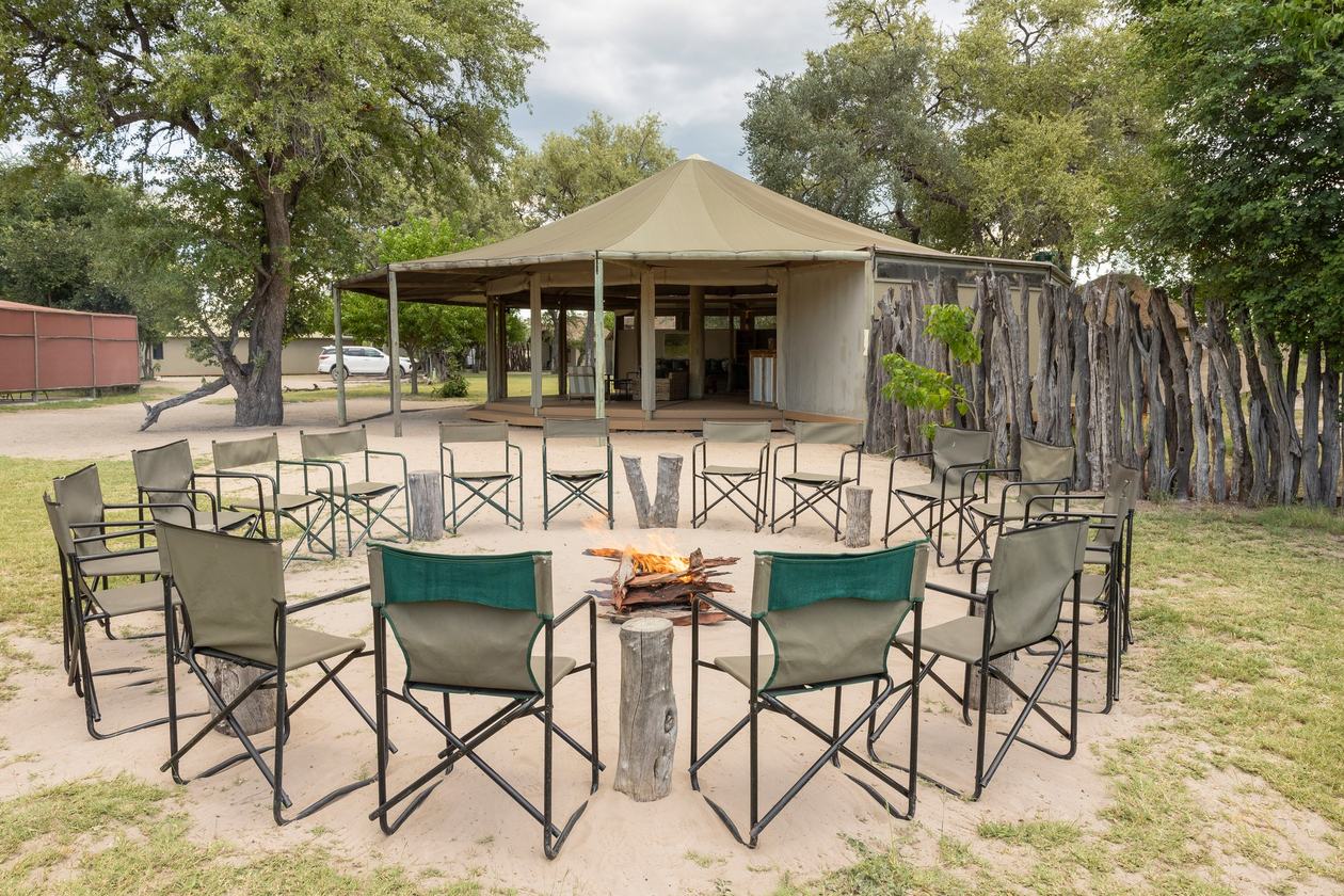 Canvas chairs circle the fire pit on the sand outside the Khwai Guest House lounge