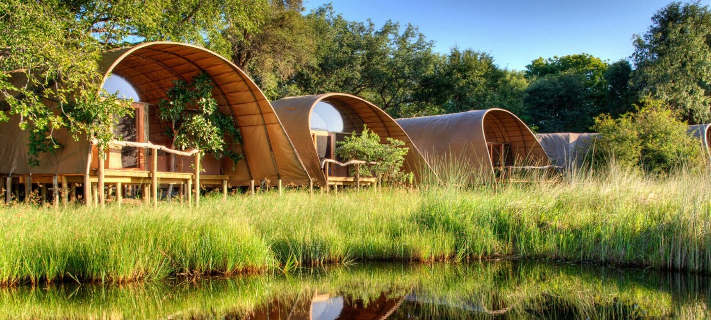 Okuti's arched canvas-and-reed chalets stand on stilts above reeds at the water's edge