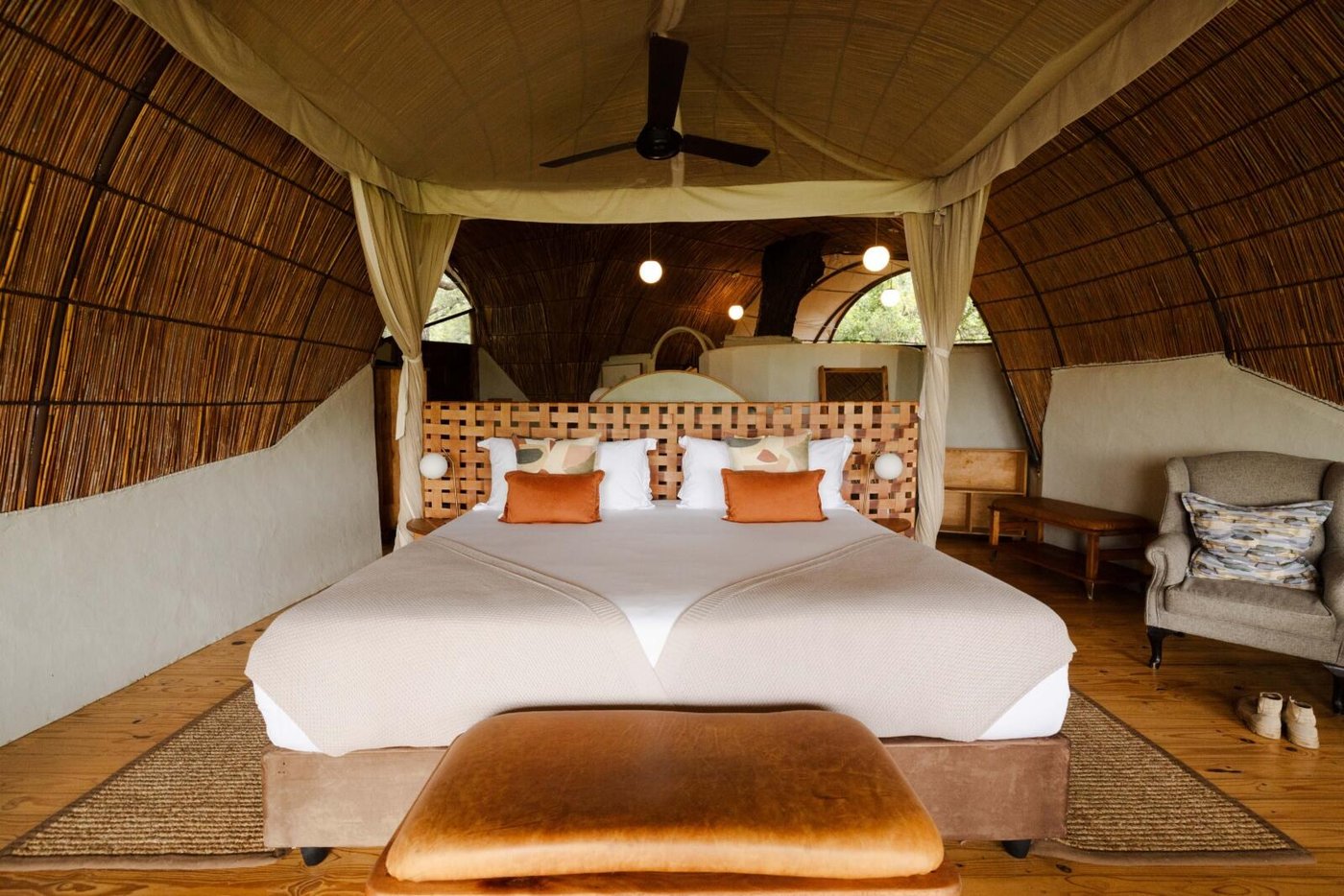 Inside an Okuti chalet: a king bed beneath a curved ceiling of woven reed