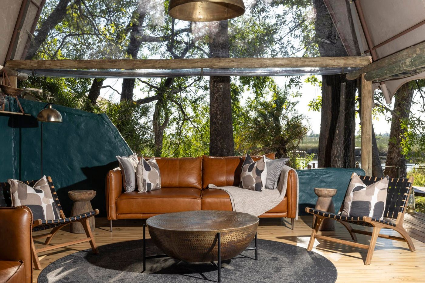 Leather sofa and woven chairs in the Okuti lounge, framed by tall riverine trees