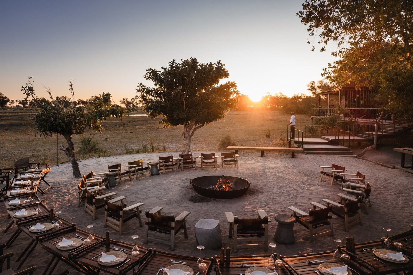 The sand boma at Qorokwe Camp at sunset, chairs ringing a fire bowl beside Moremi