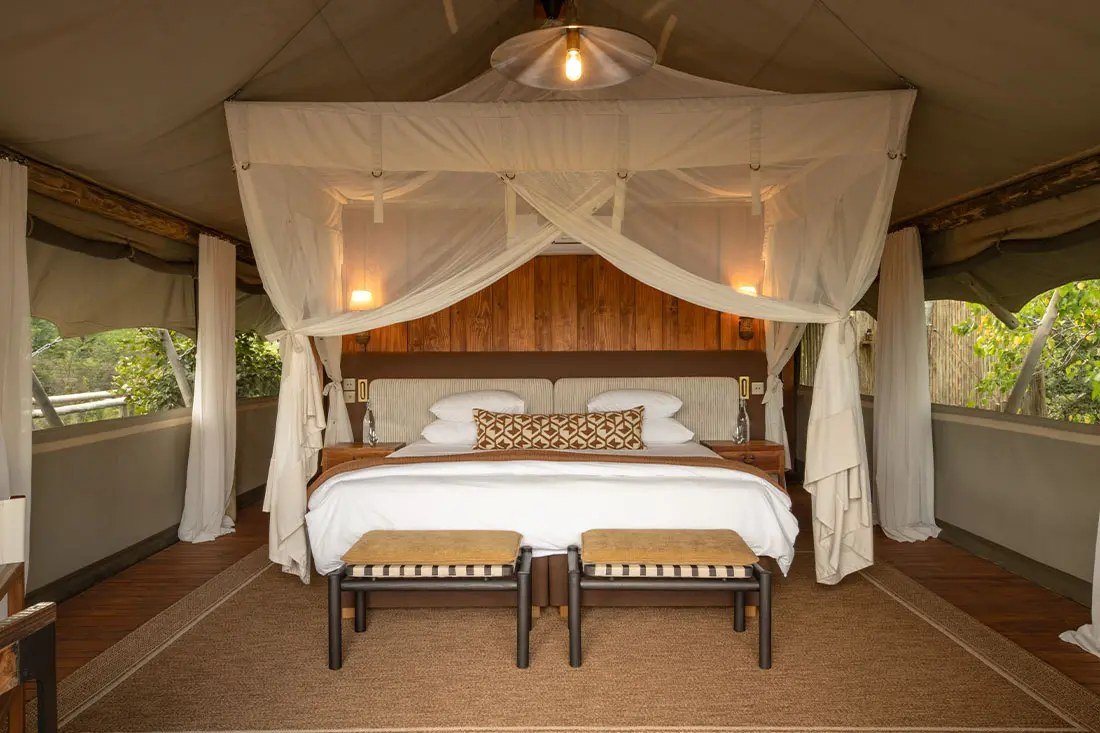 A netted king bed with a timber headboard inside a Sable Alley guest tent