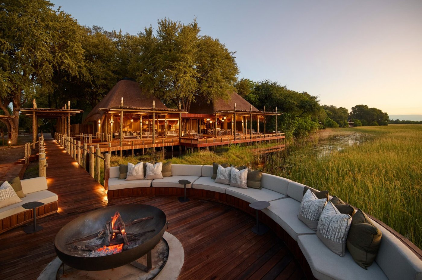 Thatched lodge and curved fire-pit lounge over the floodplain at dusk at Sediba Sa Rona, Moremi