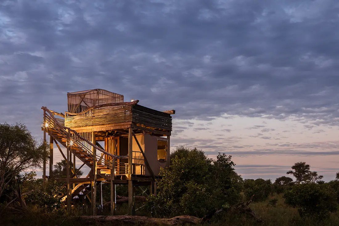 A three-storey Skybeds platform lit at dusk, its netted bed on the open top deck