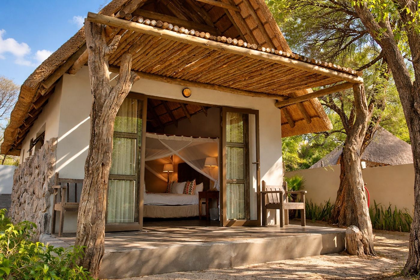 Thatched chalet with bed visible through open doors at Thamalakane River Lodge, Moremi