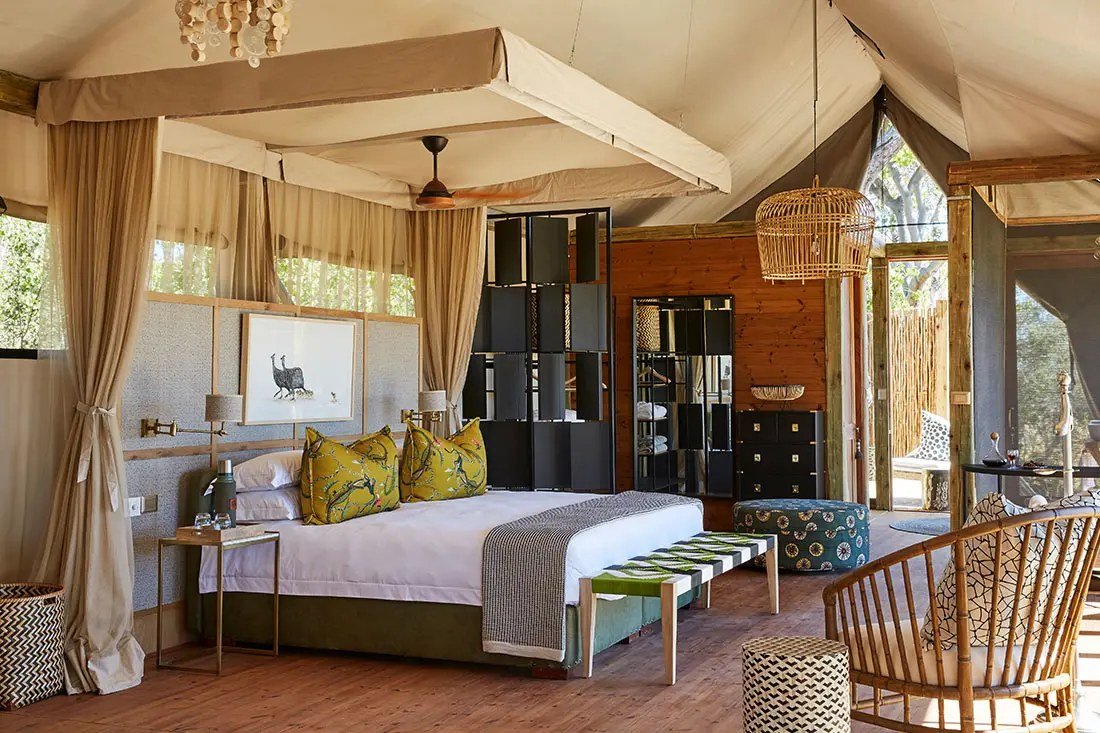 Bed with green bird-print cushions under a canvas ceiling in a Tuludi suite